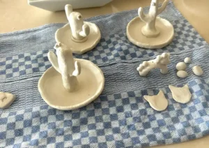 Small handmade clay dishes and decorative figures drying on a blue patterned cloth.